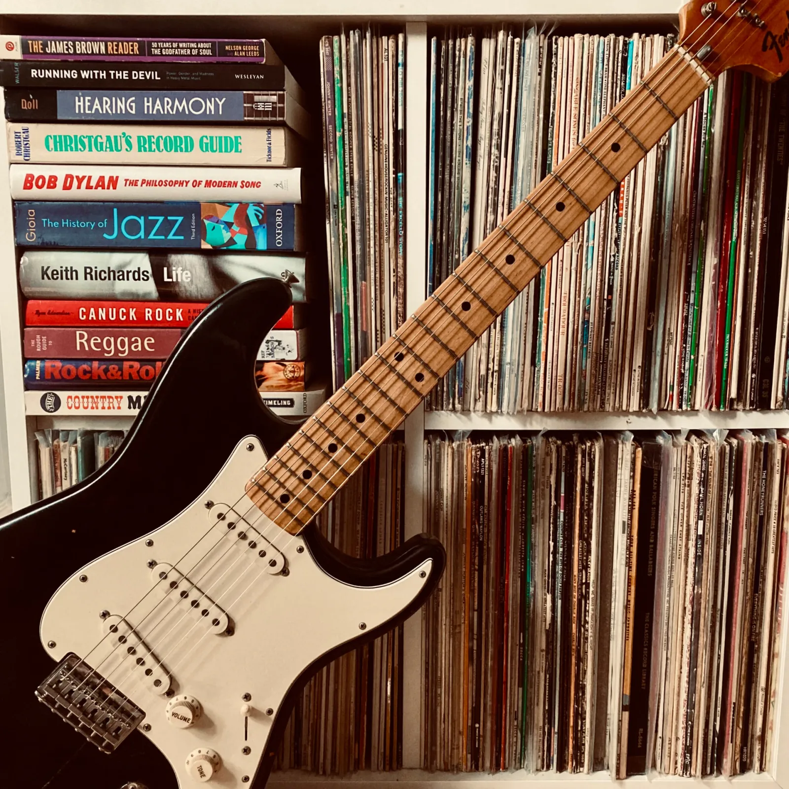 Electric guitar leaning against a shelf of records and music books